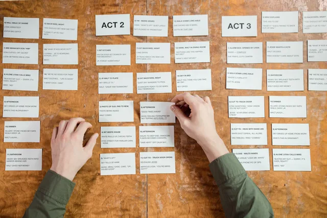 Hands arranging screenplay cards on a wooden table, depicting script development. Business video scripts and storyboards