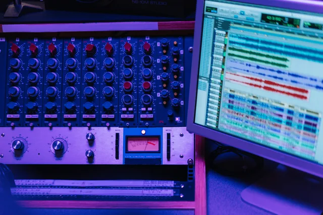 Close-up of a mixing console and screen in a recording studio, showcasing audio editing software. Fixing uneven dialogue levels during editing