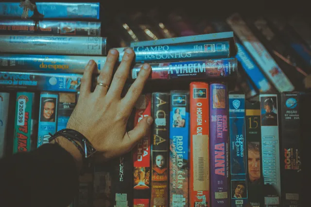 A hand reaching for a classic VHS tape from a colorful vintage collection indoors. Repurposing a business video library