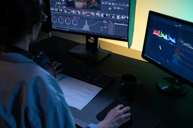 A video editor using dual monitors for editing footage in a dimly lit studio. Video production budgets and schedules